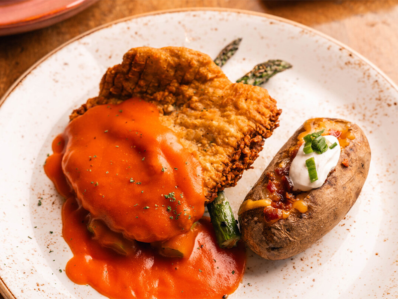 a plate with fried chicken and a baked potato on a wooden table